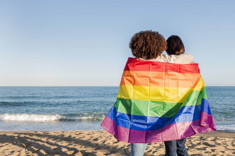A couple wrapped in a Pride flag on a beach in Puerto Vallarta